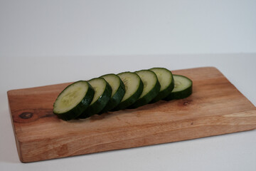 Fresh cucumber slices rest on a wooden cutting board. Simple, clean background enhances visual appeal. Perfect for healthy eating or cooking concepts. Natural texture and color highlight freshness © Nurma