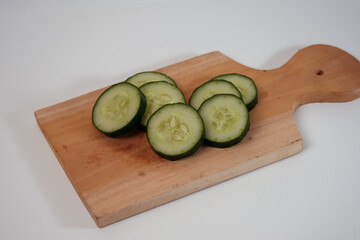 Fresh cucumber slices rest on a wooden cutting board. Simple, clean background enhances visual appeal. Perfect for healthy eating or cooking concepts. Natural texture and color highlight freshness © Nurma