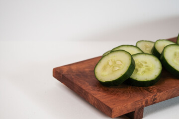 Fresh cucumber slices rest on a wooden cutting board. Simple, clean background enhances visual appeal. Perfect for healthy eating or cooking concepts. Natural texture and color highlight freshness © Nurma