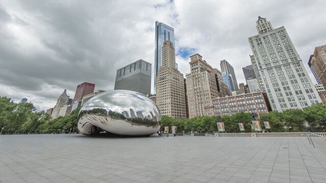CHICAGO, IL, JUN 18, 2026: Wide low-angle view of Millennium Park plaza and Cloud Gate sculpture, with a blue glass tower, ornate stone high-rises and green trees beneath a cloudy sky in Millennium Pa
