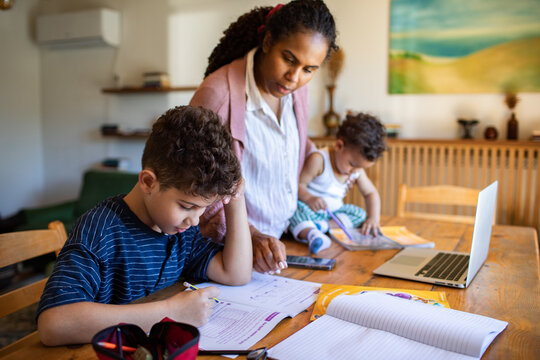 Mother helping son with homework while watching toddler