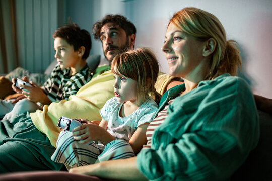 Children playing console game as parents watch on sofa