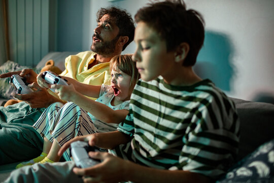 Man and kids playing video games on couch at home