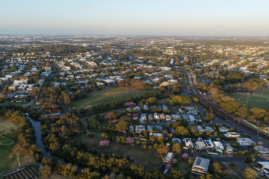 Aerial view of the residential suburb of Norman Park, featuring lush greenery, flowering trees, and a railway line winding through the landscape in Norman Park, Queensland, Australia.