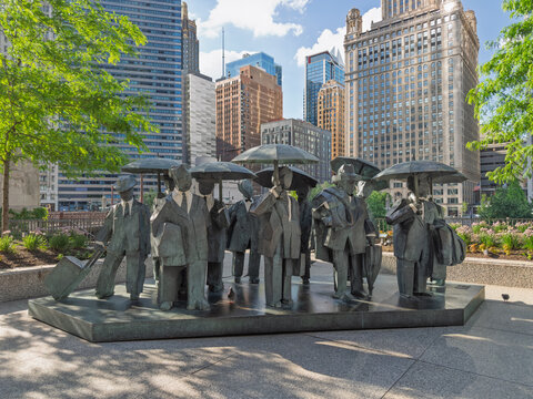 CHICAGO, IL, JUN 19, 2026: Bronze sculpture "Gentlemen" by artist Ju Ming, of a group of commuters,  with umbrellas, briefcases and luggage on a stone plaza, with Chicago high-rises and flowers behind