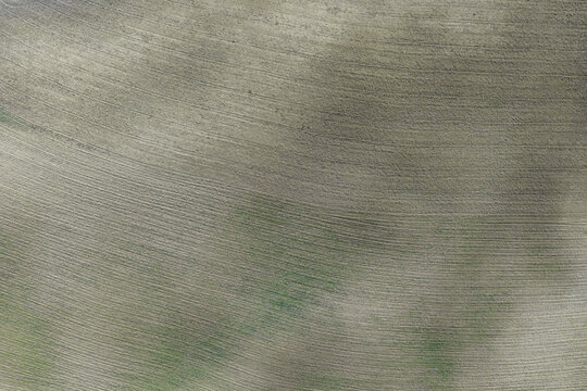 Aerial view of a freshly plowed field with textured soil patterns and subtle green vegetation in San Quirico d'Orcia, Tuscany, Italy.