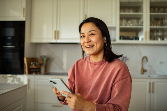 Smiling woman video calling on smartphone in home kitchen