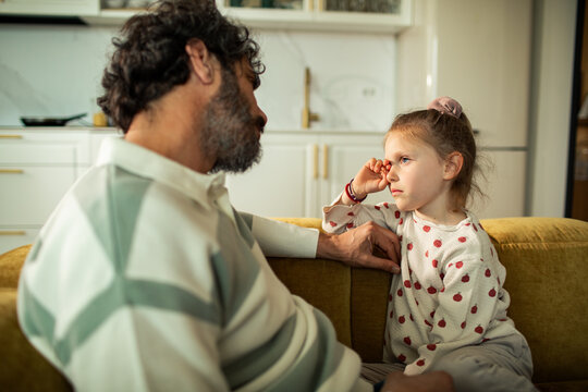 Father comforting upset daughter on living room sofa