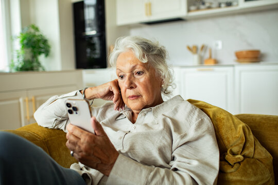 Senior woman reading phone on couch at home