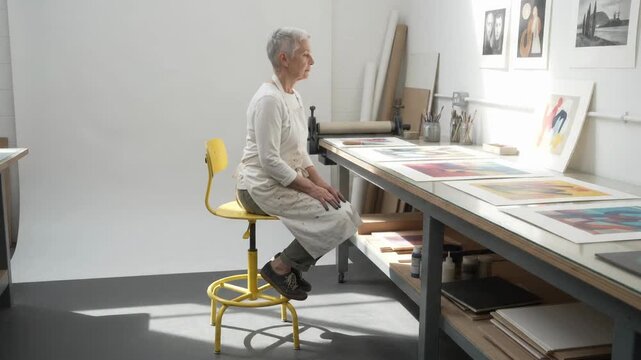 Senior Female Artist Sits Down on a Stool in Her Art Studio
