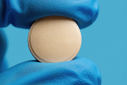 Closeup of gloved hand holding round metformin tablet. Medical worker in blue nitrile glove shows diabetes medication pill. Healthcare pro presents pharmaceutical drug for blood sugar control. Doctor