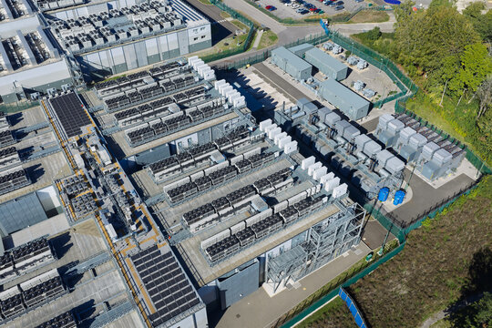 Aerial view of a large data center facility featuring rows of industrial cooling units, complex HVAC infrastructure, and a secure fenced perimeter in the United Kingdom.