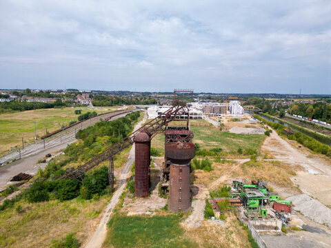 Aerial view of the historic Clabecq industrial site featuring rusted blast furnace structures, green fields, a nearby canal, and modern development in Tubize, Wallonia, Belgium.