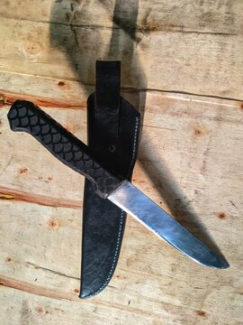 Sharp steel knife with black leather sheath on rustic wooden background