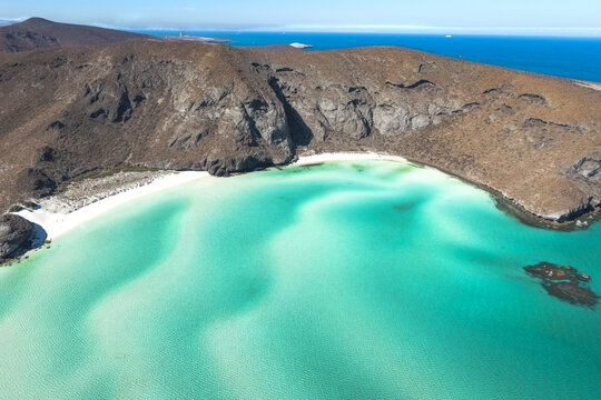 Aerial view of the turquoise waters and white sand beach of Playa Balandra surrounded by arid rocky hills in La Paz, Baja California Sur, Mexico.