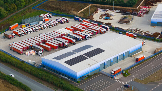 Aerial view of industrial logistics warehouses with numerous HGVs parked in the yard, featuring solar panels on the roof in Bury St Edmunds, England, United Kingdom.