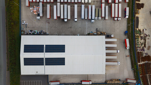 Aerial view of industrial logistics warehouses with solar panels on the roof and numerous HGVs parked in the loading bays in Bury St Edmunds, England, United Kingdom.