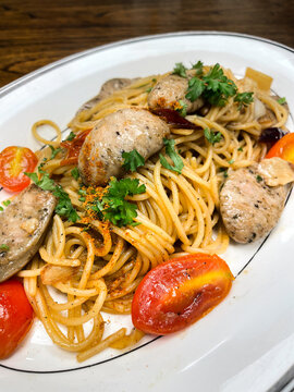 Delicious spaghetti &lsquo;aglio e olio&rsquo; or Italian sausage, cherry tomatoes, garlic, chili, and fresh parsley served on a white plate on wood table.