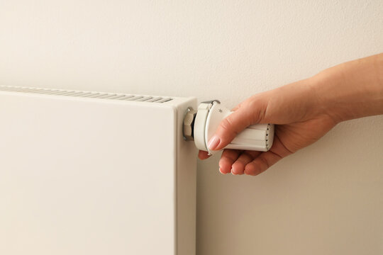 A hand is turning the valve on a white radiator for warmth