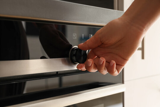 Hand adjusting the oven temperature dial in a stylish kitchen