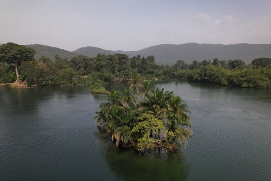 Aerial view of a small island covered in palm trees situated in the middle of the Volta River, surrounded by lush green banks and rolling hills in Akosombo, Eastern Region, Ghana.