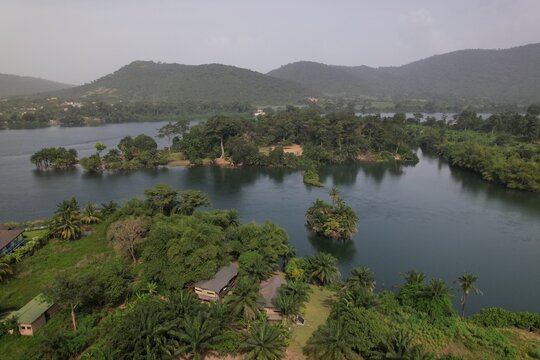 Aerial view of the Volta River near Akosombo, featuring lush islands, dense tropical vegetation, and small buildings nestled along the shoreline in Akosombo, Eastern Region, Ghana.