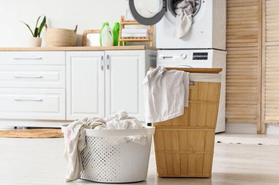 Laundry day and household chores, dirty clothes in plastic basket and wooden hamper with washing machine in modern home interior