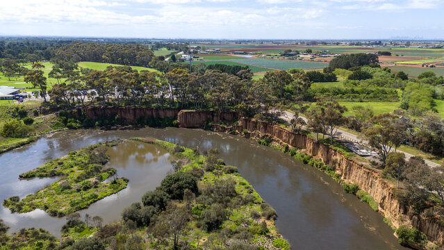 Aerial drone view of the K Road Cliffs at Werribee South, Melbourne, Victoria, Australia, with a tall eroded cliff face curving above a bend of Werribee River, eucalyptus trees along the clifftop.