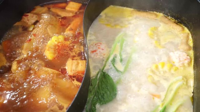 A close-up view of a split hot pot with spicy red broth and mild white broth boiling together in a restaurant setting.