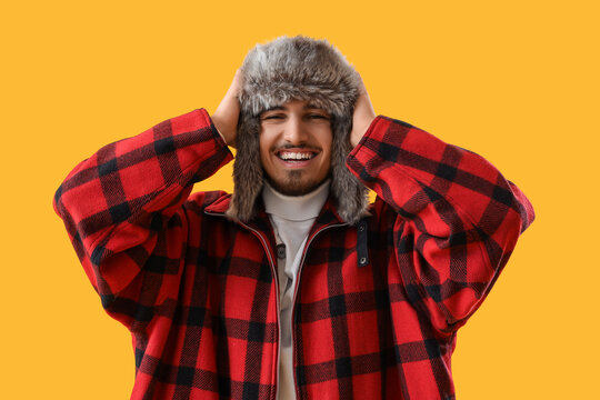 Winter fashion and seasonal joy, happy young man wearing a red plaid jacket and fur trapper hat laughing on a bright yellow background