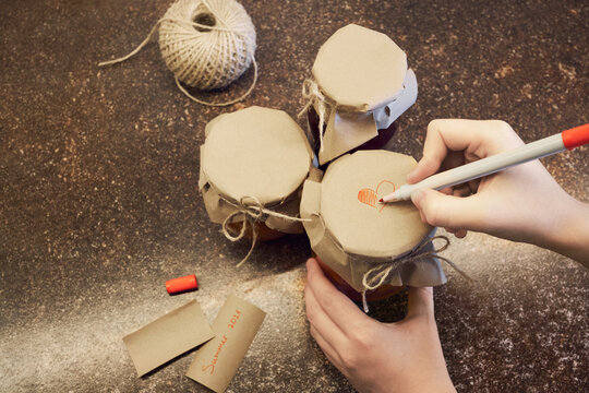 Hand decorating jar of homemade jam with heart, preparing thoughtful gift