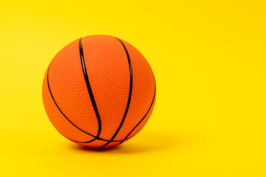 A textured orange basketball with black seams rests on a solid yellow studio backdrop, leaving open space for text. A sporty concept of team games, fitness and active leisure.