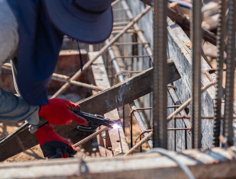 Welder using an electric arc welding torch to connect reinforcing steel bars within a formwork structure.