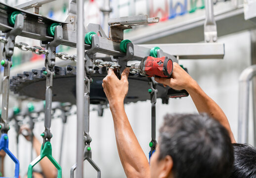 Close-up of a worker's hands assembling metal chain components and trolley hangers on an automated production line