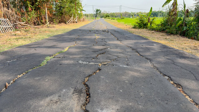 Cracked damaged asphalt road in rural village countryside area