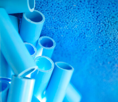 Blue PVC pipe and plastic polymer pellets shown as raw material for industrial pipe production. Thermoplastic resin, petrochemical processing, extrusion technology and manufacturing.