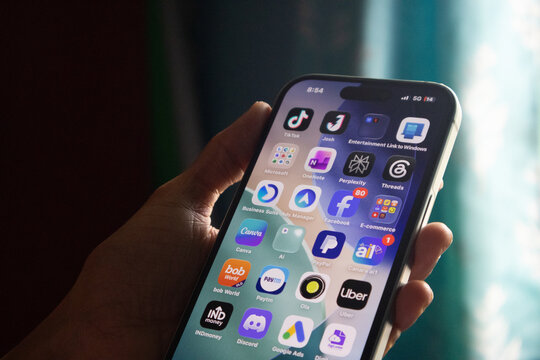 Smartphone display featuring tiktok threads and perplexity ai icons held in hands against soft background.