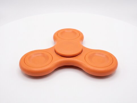 Orange fidget spinner low angle view on white background, matte plastic stress relief toy