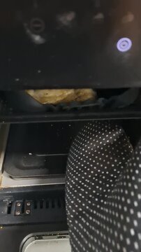 Seasoned chicken cooks inside an air fryer basket in a home kitchen, with a person checking the cooking process through the open appliance