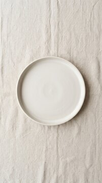Minimalist White Plate on Textured Linen Fabric Background.