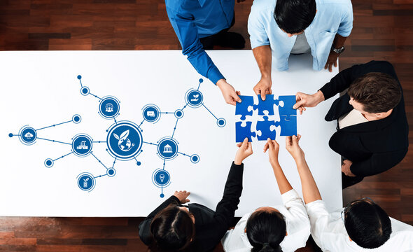 A diverse team collaborates around a table, piecing together a puzzle while discussing a green business strategy. Icons symbolize technology and sustainability efforts. Amity
