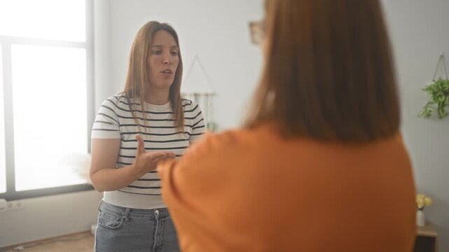 Woman gesturing with hand while speaking to another woman in a livingroom, palms visible and expressive body language during a domestic conversation; family tension.