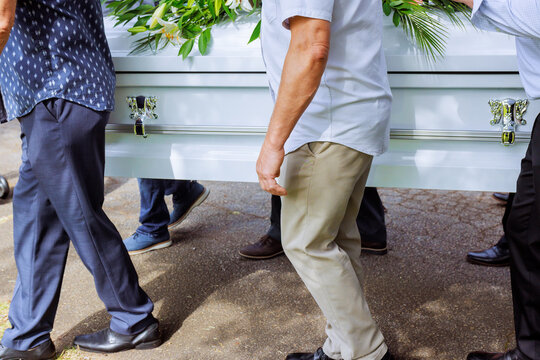 People carry white coffin surrounded by greenery in somber setting