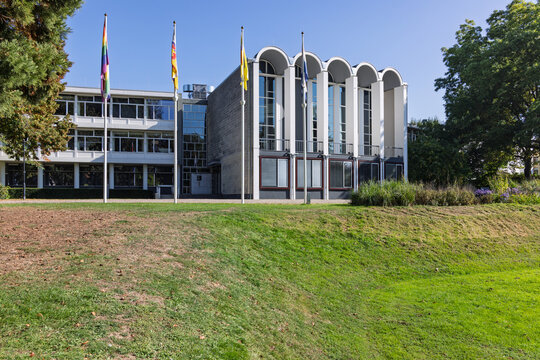 Valkenburg, Netherlands. Modern town hall building with flags and green lawn under a clear blue sky, presenting municipal architecture.