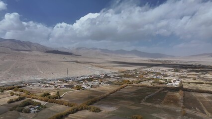 Fototapeta premium Aerial view of a village and farmland in the Xinjiang plateau valley surrounded by mountains