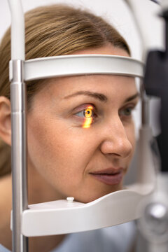 Closeup female patient during professional eye examination with slit lamp microscope. Bright diagnostic light highlights pupil for ophthalmic assessment, vision correction and eye disease prevention