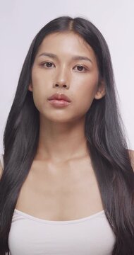 Young Asian woman posing in beauty studio. She holds her hands near face and looks at camera.