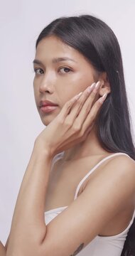 Asian woman dropping serum on cheek with dropper and smiling. She gently massages serum into face.