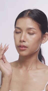 Asian woman gently massaging her cheeks with fingers. She looks at camera showcasing smooth skin.