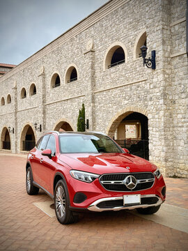 Front view of a red 2026 Mercedes-Benz GLC 300 SUV, parked on a picturesque street, in a Catalonian style village.